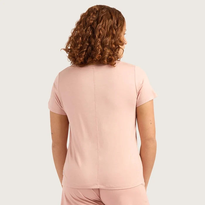 A close-up of a woman wearing a light pink short-sleeve crewneck t-shirt against a solid light gray background.