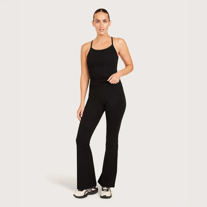 A woman modeling black flare pants, standing against a light gray studio background.