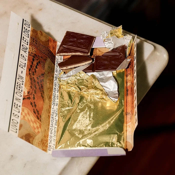 Open packet of Luvio hazelnut truffle bar with luxury packaging, gold foil on a marble surface with red silk in the background.