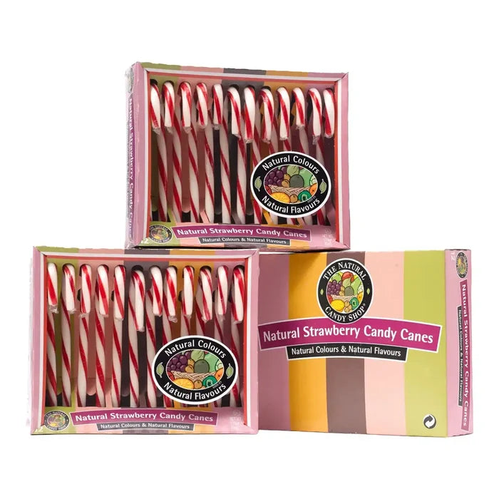 Three boxes of natural strawberry candy canes stacked together on a white background. The pink boxes contain red and white striped candy canes, and the front box features a colorful pastel design with the brand logo 'The Natural Candy Shop'.