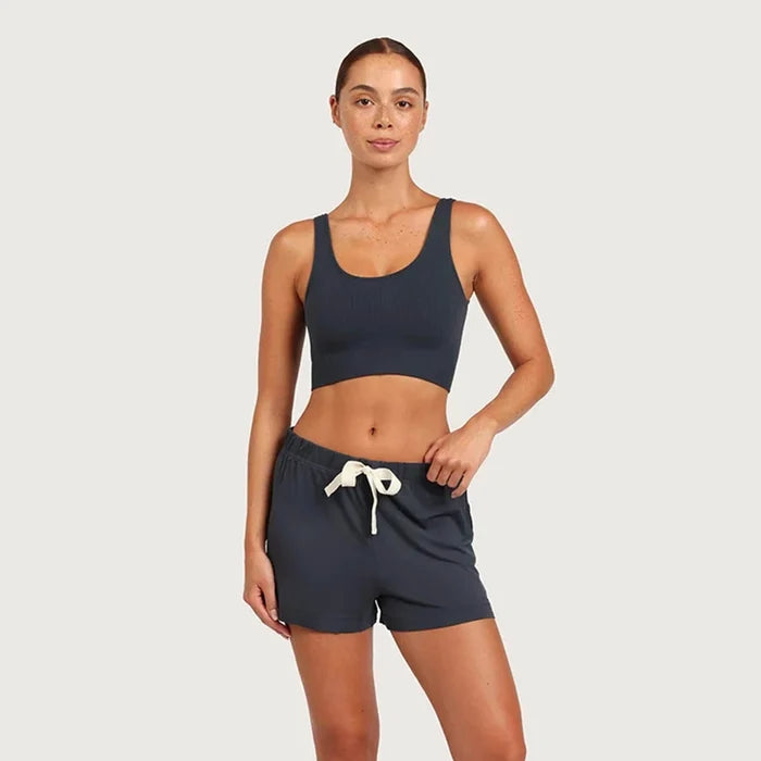 A woman modeling a matching two-piece activewear set consisting of a dark navy scoop-neck crop top and matching dark navy shorts with a white drawstring, set against a solid light gray background.